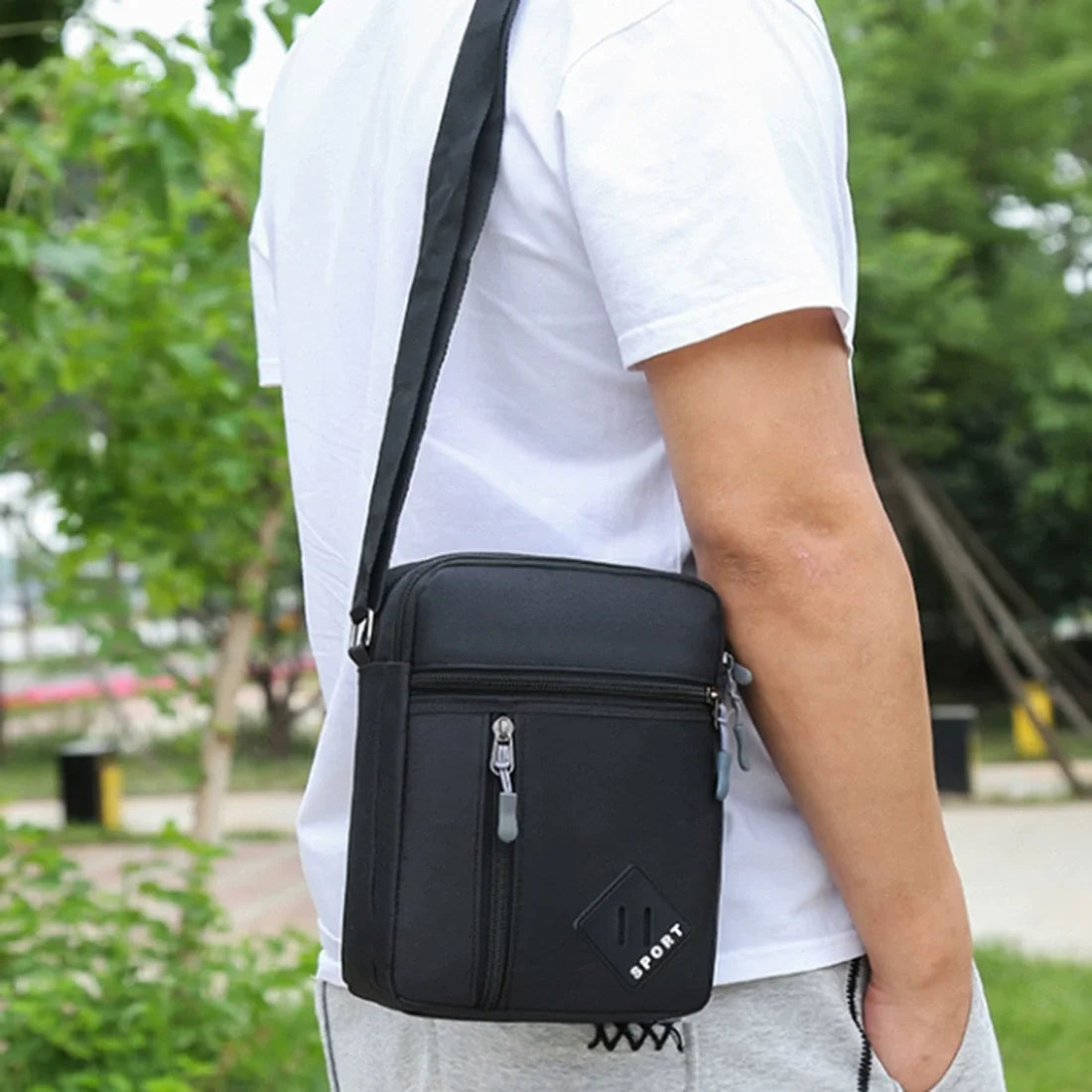A man wearing a white t-shirt is holding a black lightweight crossbody sling bag with multiple zip pockets.
