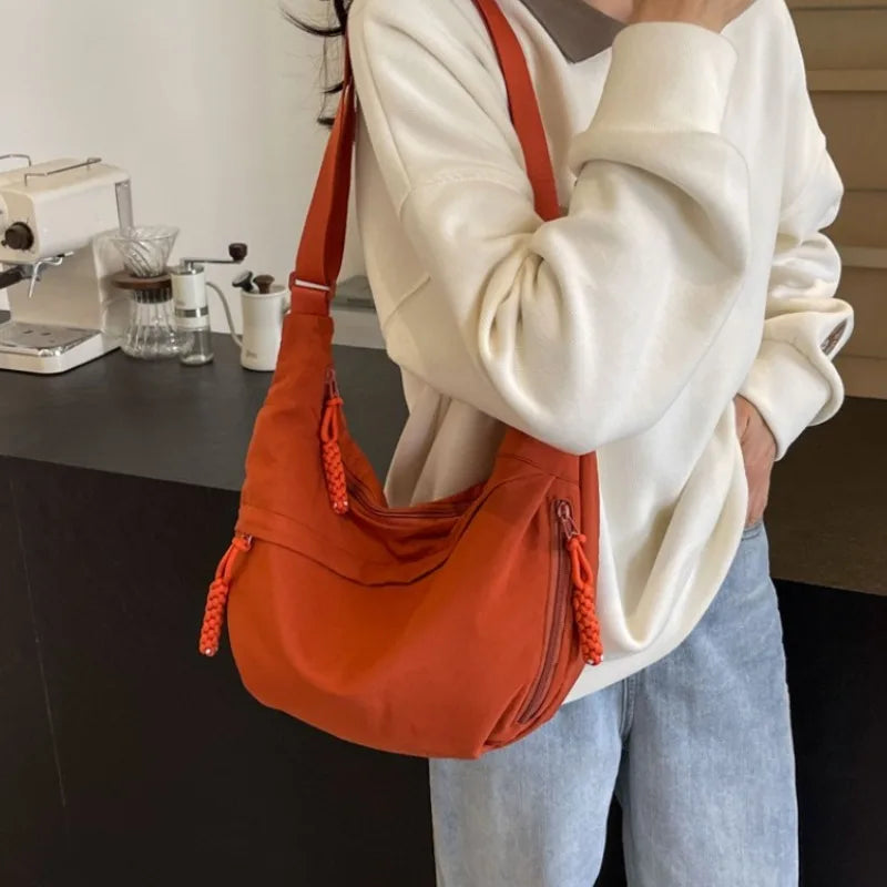A person is holding an orange nylon crossbody bag with a strap against a light background.