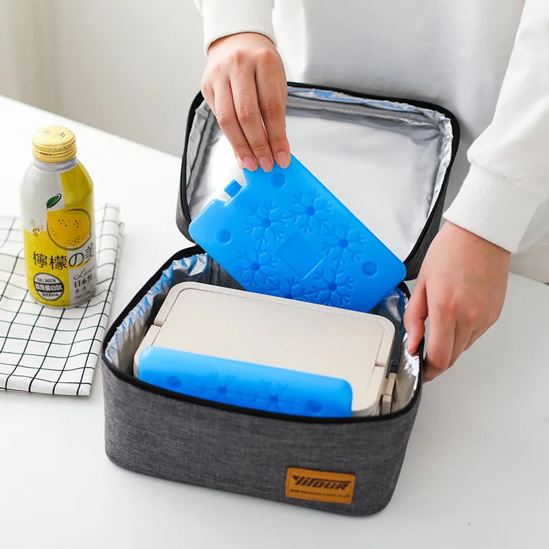 A hand is opening a gray reusable ice pack containing a blue silicone leak-proof ice pack and a yellow bottle on a white tabl