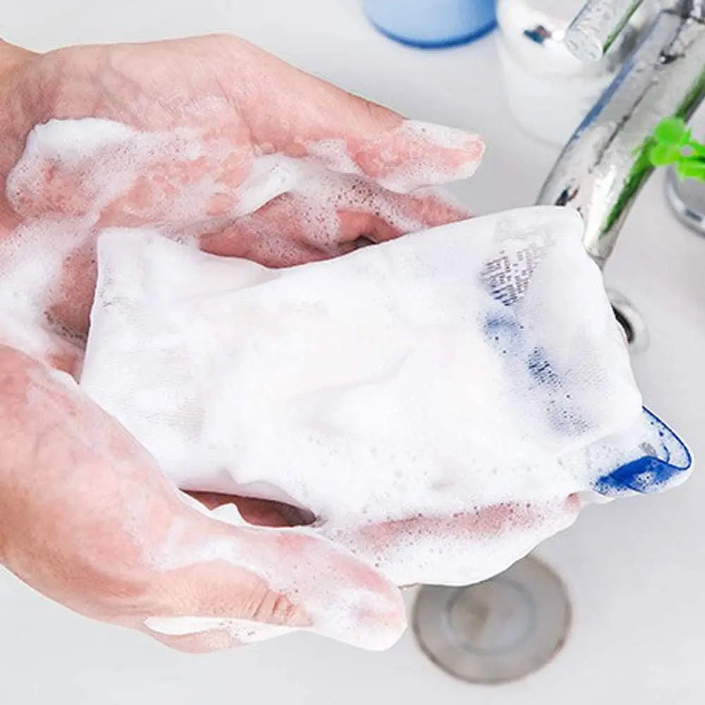 A hand is squeezing a white foaming mesh bath pouf with a blue hanging loop.