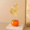 Gold-toned Nordic ceramic sculpture shaped like a stylized leaf resting on an orange spherical base.
