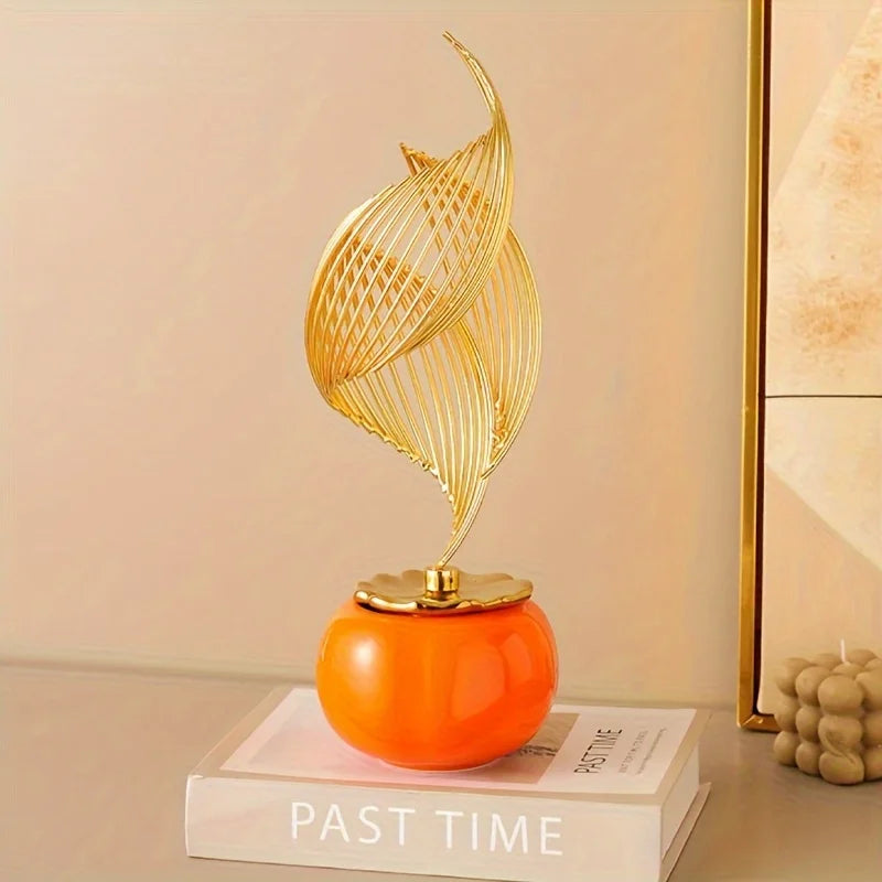 Gold-toned Nordic ceramic sculpture shaped like a stylized leaf resting on an orange spherical base.