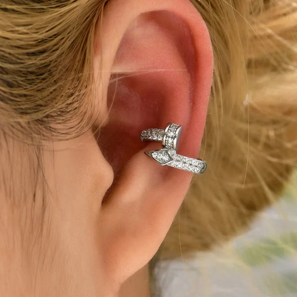 Aretes de zirconio geométricos plateados puestos en la oreja de una persona.