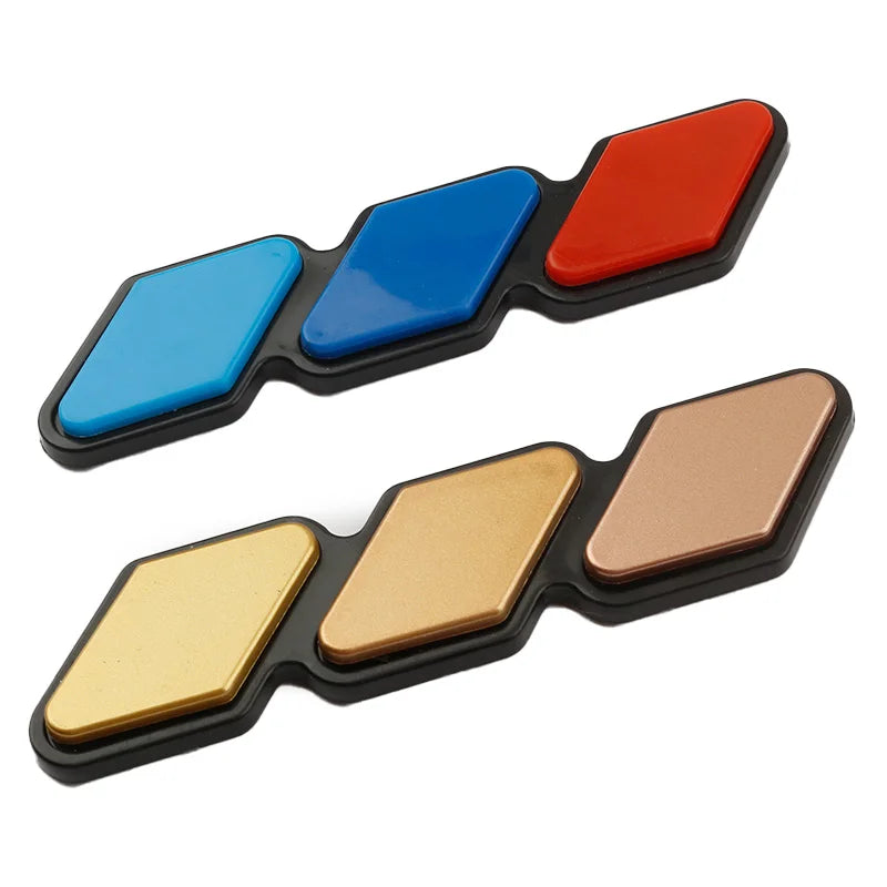 A set of three colored grille emblem stickers in red, blue, and gold on a black background.