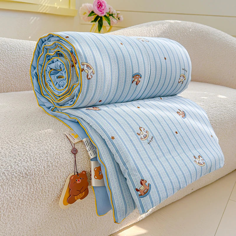 Light blue and white striped quilt with playful cartoon animal prints resting on a beige sofa.
