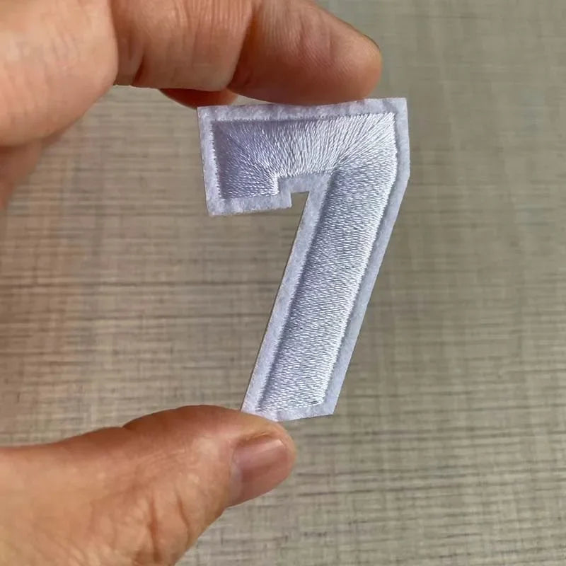 A hand holds a white iron-on 3D number patch shaped like the numeral seven.