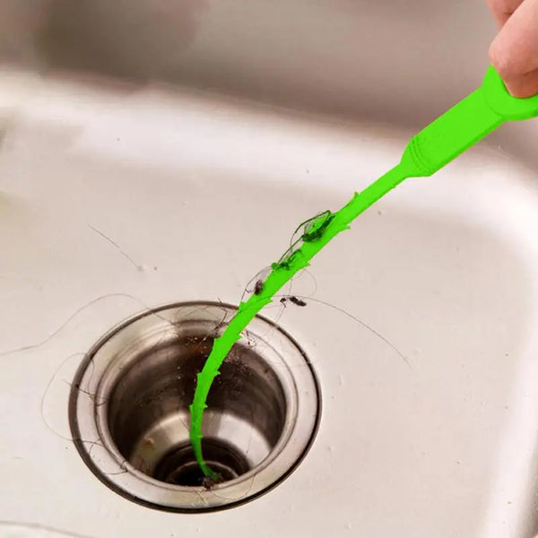 Una mano usa una serpiente de drenaje flexible verde brillante para limpiar un atasco en el desagüe de un fregadero.