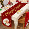 A festive red table runner with gold lettering and Christmas designs is displayed on a white table.