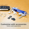A blue aluminum key clip with a carabiner hook and various metal keys and accessories on a wooden surface.