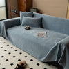 A light blue herringbone chenille sofa throw draped over a sofa with matching pillows and a decorative tassel edge.