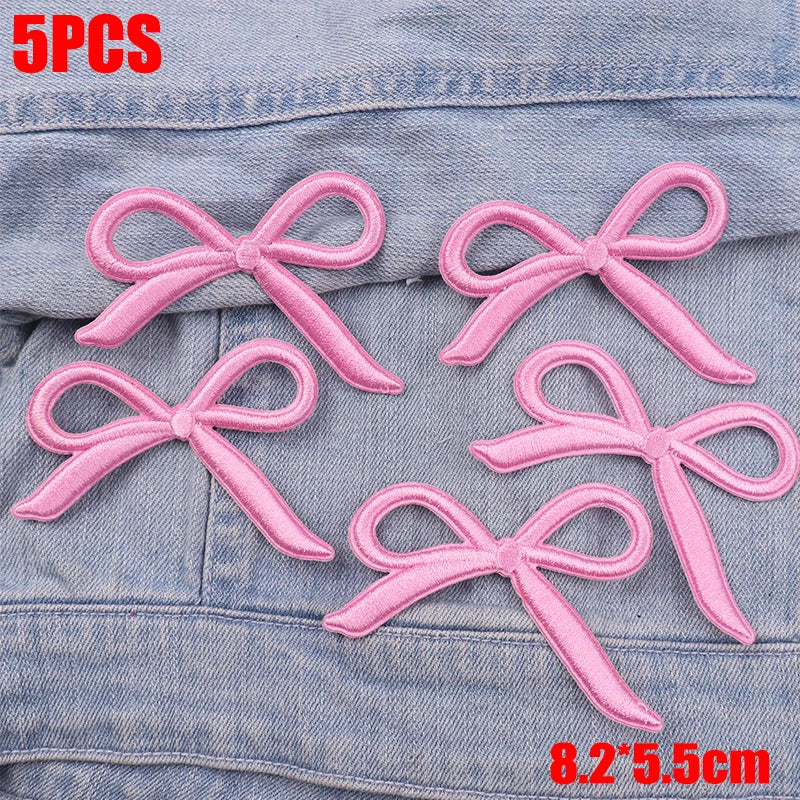 Five pink embroidered bow iron-on patches displayed on a denim fabric.