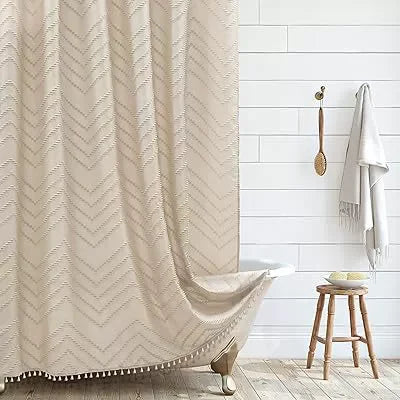 A beige boho waterproof shower curtain with tassels and hooks hanging against a white tiled wall.