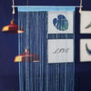 A blue beaded string curtain hangs vertically, featuring a white rectangular sign with the word LIVE and a blue leaf design.