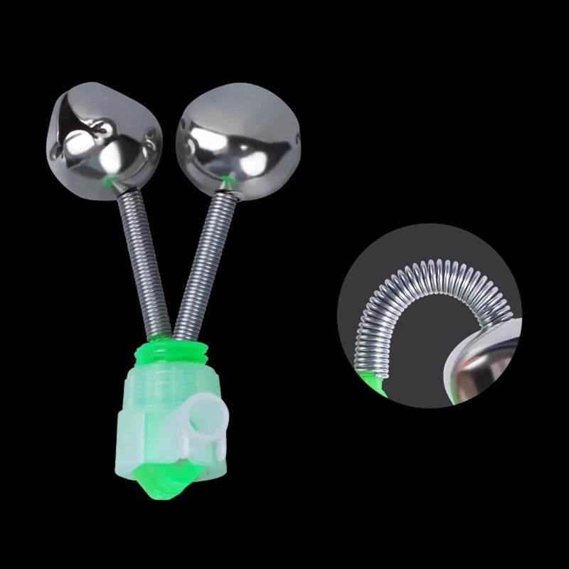 A close-up view of a fishing rod bite alarm bell with a silver sphere and a green clip-on indicator.