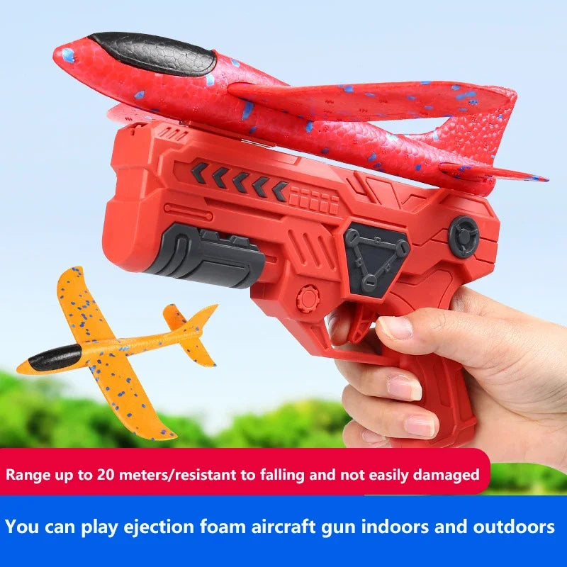 A hand holds a red foam glider aircraft gun toy, ready to launch, with an orange airplane visible nearby.