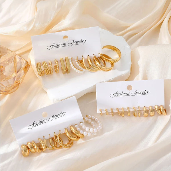 Goldene und Perlenohrringe auf weißen Karten vor cremefarbigem Stoff.