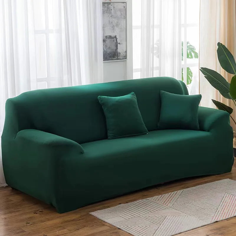 A deep emerald green elastic stretch sofa cover for a 3-seater sofa placed in a bright living room.