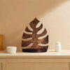 A dark brown wooden wall-mounted storage rack shaped like a tropical leaf, displayed on a light wooden surface.