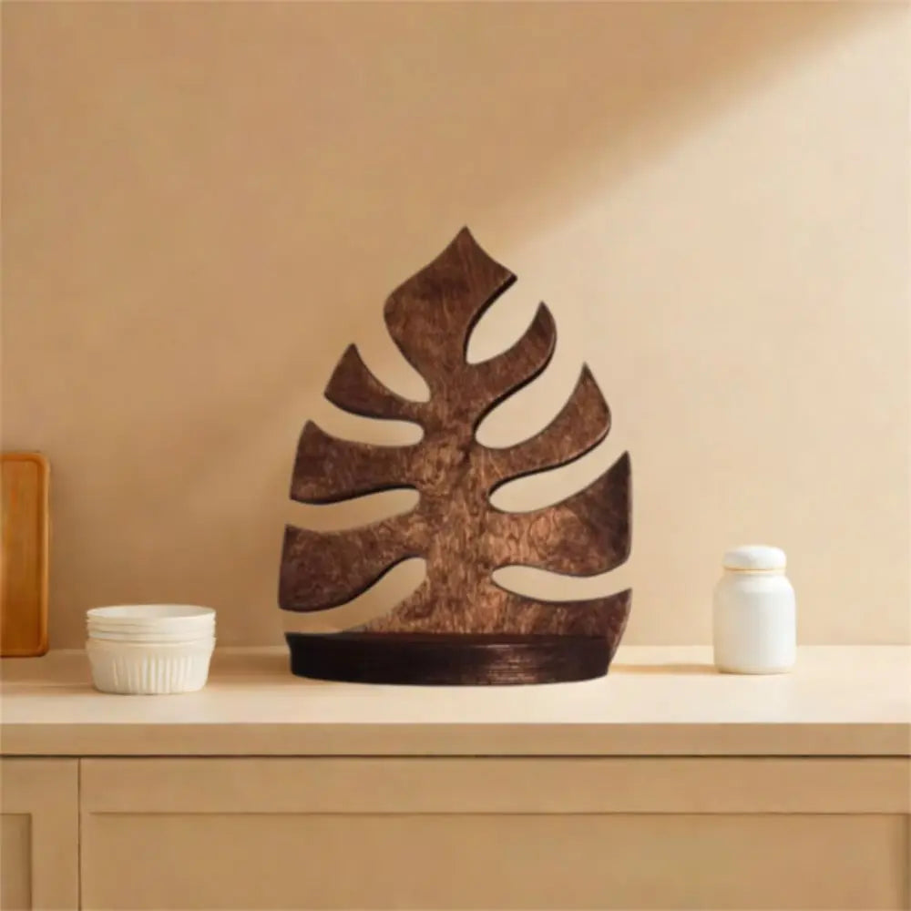 A dark brown wooden wall-mounted storage rack shaped like a tropical leaf, displayed on a light wooden surface.