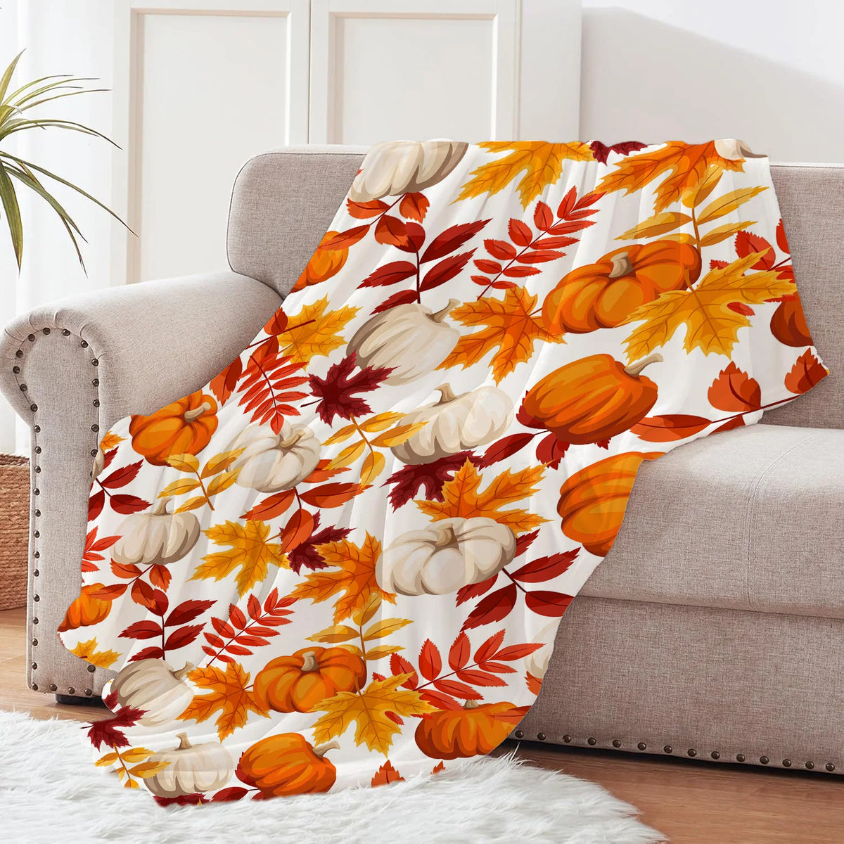 An orange and yellow maple leaf pattern flannel throw blanket draped over a light gray sofa.