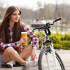 A young woman sits on a bicycle with a yellow cup, looking to the side.
