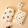 A soft cotton gauze baby swaddle blanket with brown bear patterns is displayed next to a fluffy white pom-pom.