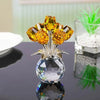 A crystal rose sculpture features a reflective bouquet of yellow-orange crystals on a clear base.