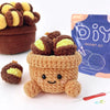 A brown crocheted animal figure sits in a pot next to a purple DIY crochet kit bag.
