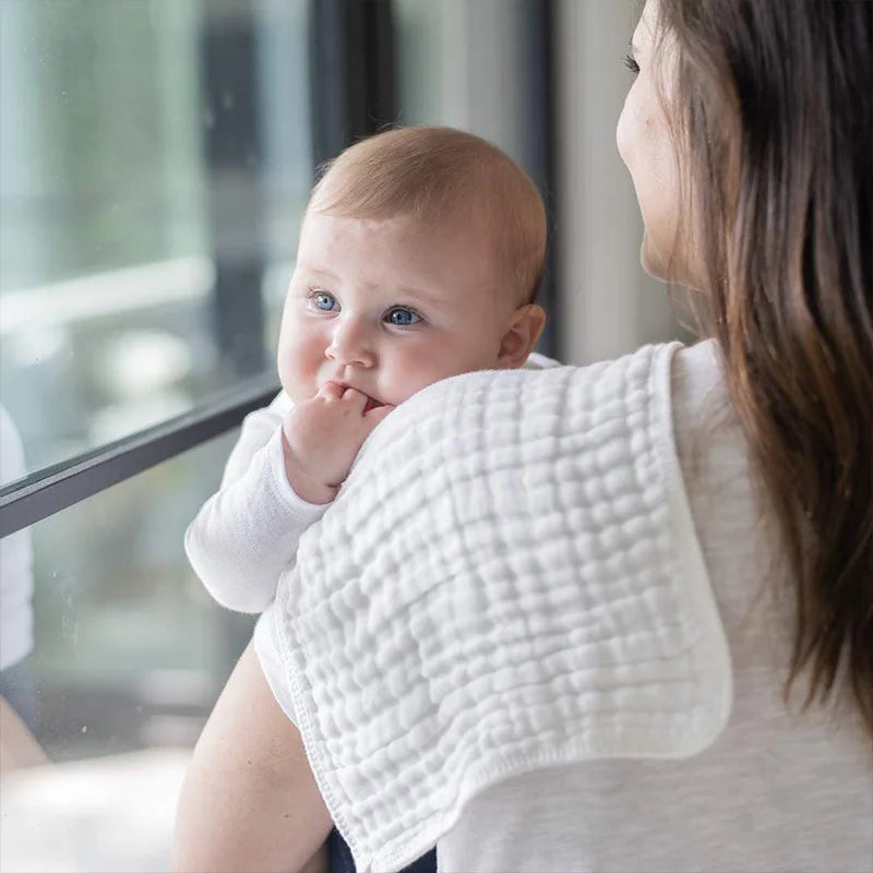 A woman holds a baby with a white muslin burp cloth against her shoulder.