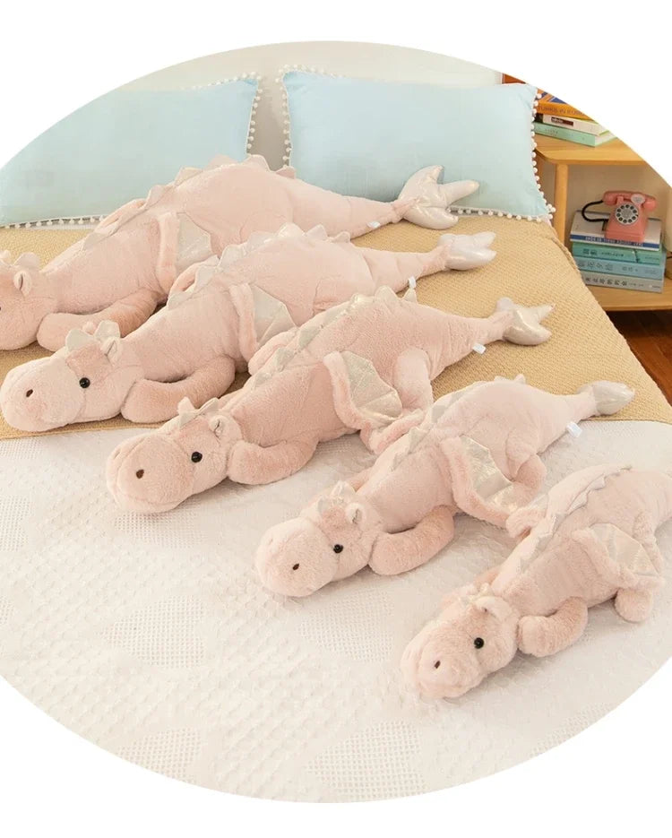 A collection of soft pink and beige dragon plush pillows arranged on a light-colored surface.