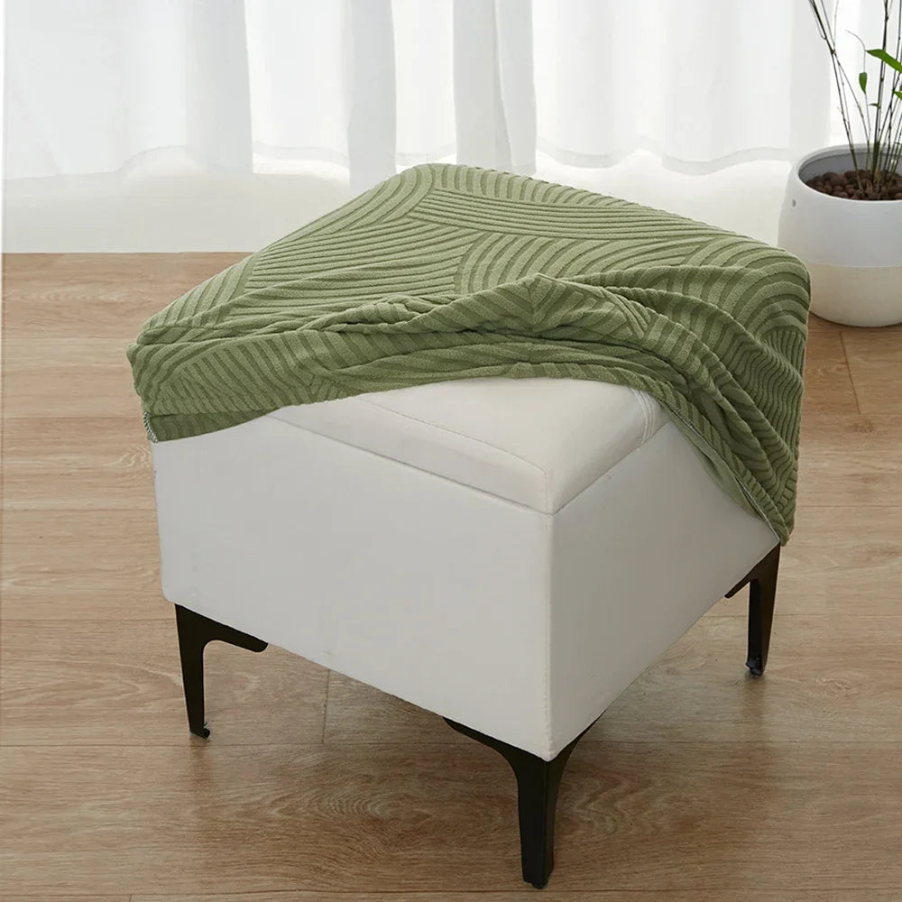 A light green geometric jacquard stretch ottoman cover draped over a white upholstered ottoman.