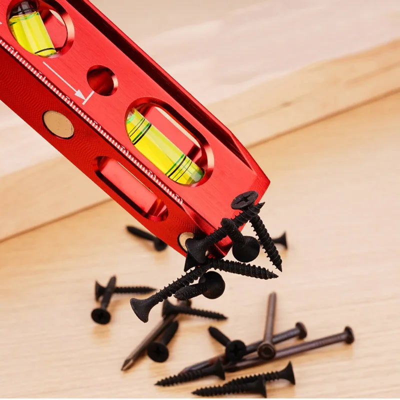 A red magnetic aluminum level ruler with V-grooves is shown on a wooden surface, with several small black screws scattered ne