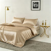 A luxurious champagne silk duvet cover set displayed on a bed with gold accents and a framed black and white photograph.