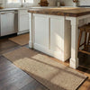 A rectangular natural fiber kitchen runner rug placed on a dark wood floor in a bright kitchen setting.