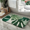 A tropical green leaf print non-slip area rug placed on a tiled floor next to a bathroom sink.