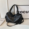 A black vintage leather tote bag with a zipper detail is displayed on a white surface next to a framed sign.