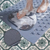 A person's feet are placed on a gray non-slip bath mat with massage nodes, creating foam.