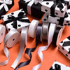 A collection of black and white polka dot gift boxes and satin ribbon rolls in various shades are displayed on an orange back