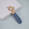 A gold-toned TPU key fob cover with a blue leather strap and a silver chain is displayed on a white surface.