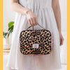 A woman holds a leopard print toiletry bag with pink trim against a white dress.