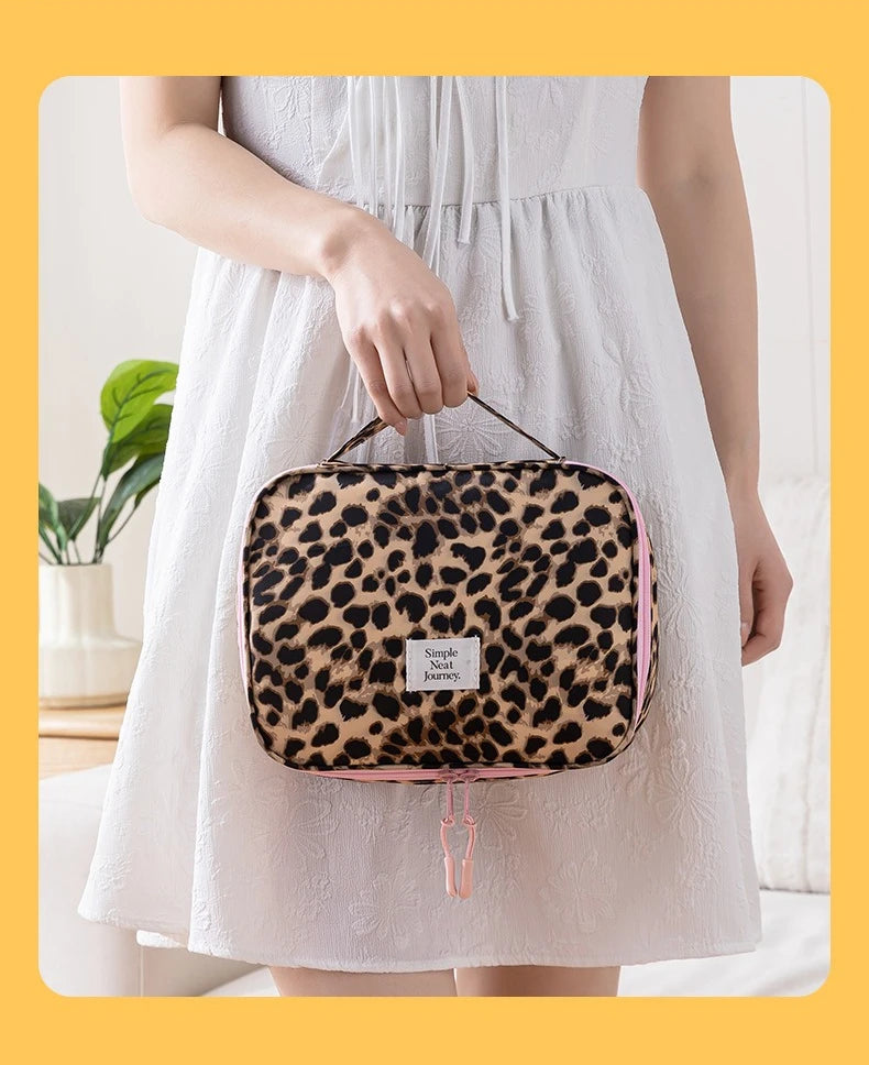 A woman holds a leopard print toiletry bag with pink trim against a white dress.