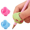 A hand holds a pink pencil with an ergonomic grip trainer, showing two different colored silicone grips for posture correctio