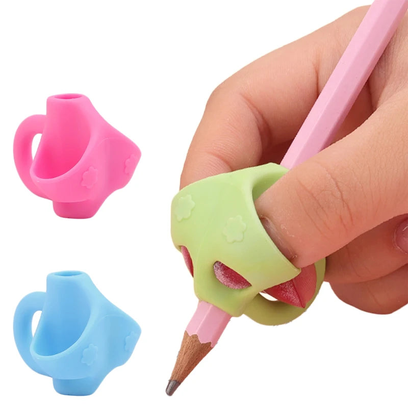 A hand holds a pink pencil with an ergonomic grip trainer, showing two different colored silicone grips for posture correctio
