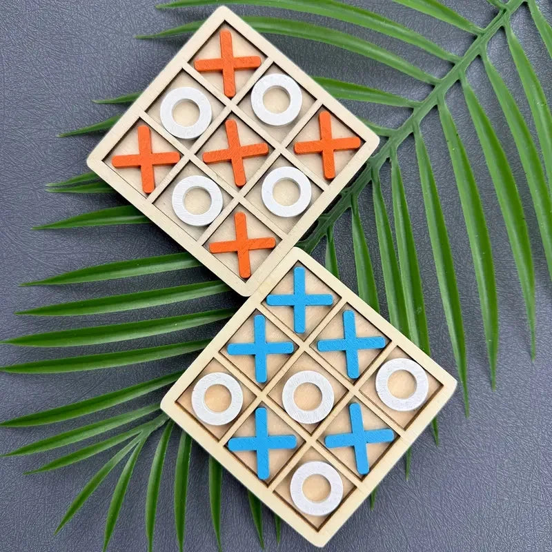 A wooden tic tac toe game set with orange and blue markers is displayed on a dark surface surrounded by green palm leaves.