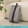 A gray and white patterned waterproof boot storage bag with a brown handle resting on a light-colored sofa.