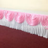 Elegant ice silk table skirt with matching top swag in pink and white fabric displayed on a red carpet.
