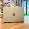 A silver Apple MacBook laptop is placed on a wooden table in a bright indoor setting.
