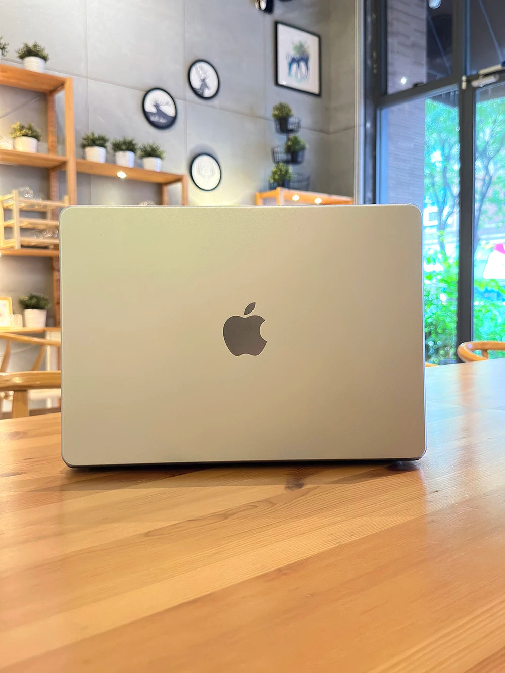 A silver Apple MacBook laptop is placed on a wooden table in a bright indoor setting.