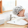 A person is using a white waterproof shower cap over their head while washing their face at a sink.