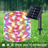 A coil of colorful fairy string lights is shown next to a solar-powered outdoor light fixture on green grass.